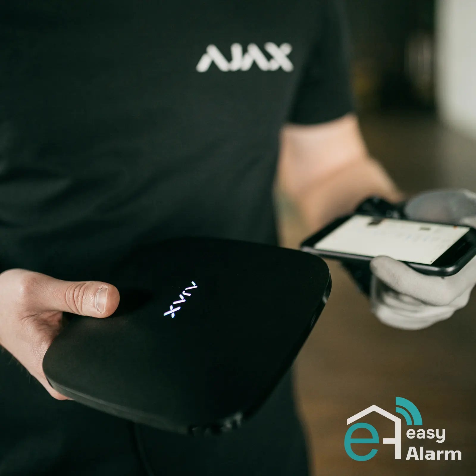un professionista Ajax ha in mano uno smartphone e un hub ajax con logo di Easy Alarm